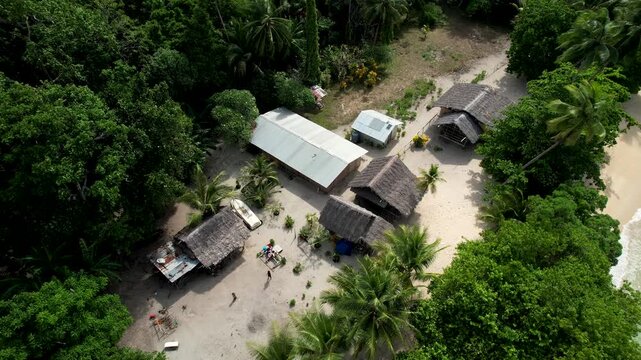 Aerial view of traditional thatched-roof huts and people in a clearing on Mushu Island surrounded by dense jungle and a sandy beach Wewak District, East Sepik Province, Papua New Guinea.
