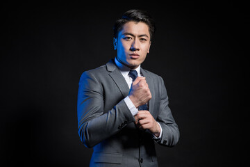 Naklejka premium Confident young businessman adjusting tie on dark background