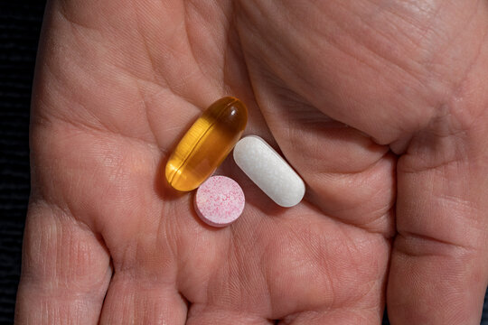 Three diverse pills and capsules in human palm. Hand holding a yellow gel capsule a white tablet and pink speckled pill representing daily health routine medication intake or medical treatment