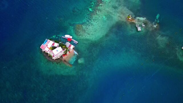 Aerial view of a luxury villa on a small rocky island surrounded by turquoise coral reefs and deep blue ocean water, Sandy Bay, Bay Islands Department, Honduras.