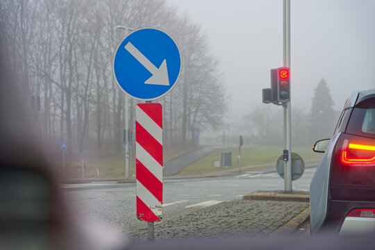 Traffic sign and red light at foggy intersection with car waiting on road