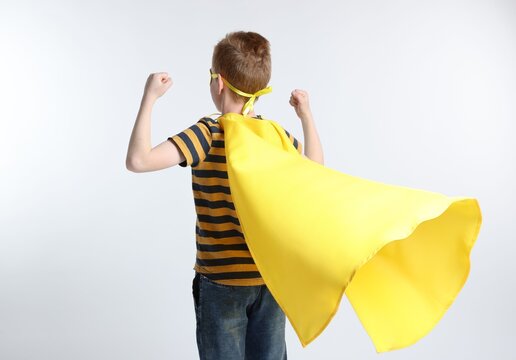 Little boy in superhero costume showing muscles on white background, back view
