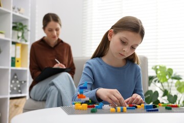 Fototapeta premium Girl playing with toys at white table during consultation with professional child psychologist indoors, selective focus