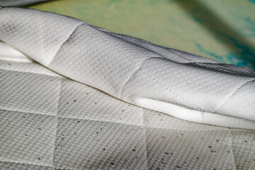 Fototapeta premium White quilted mattress with dirt stains and folded edge on a green surface