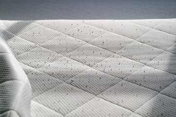 Fototapeta premium White quilted mattress surface with small dark specks and textured fabric pattern