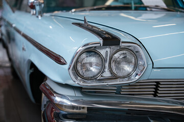 Obraz premium Detailed frontal view of classic pale blue automobile, showcasing dual round headlights, chrome grille, and shiny chrome bumper. Decorative chrome trim and hood ornament enhance vintage appeal.