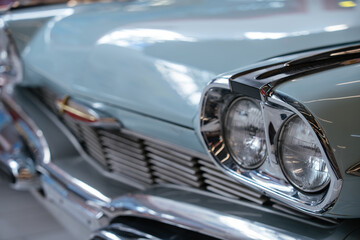 Naklejka premium Detailed close-up view of front section of light blue vintage automobile. Polished chrome headlights and grille reflect surroundings, emphasizing classic design in a softly blurred indoor setting.