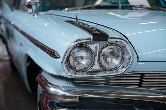 Detailed frontal view of classic pale blue automobile, showcasing dual round headlights, chrome grille, and shiny chrome bumper. Decorative chrome trim and hood ornament enhance vintage appeal.