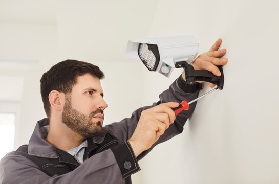 CCTV indoor wall setting, installing security camera, man holding screwdriver, fastening mount to wall, focused, performing professional installation work, ensuring building security system