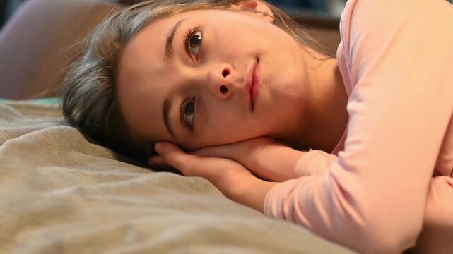 Happy preteen girl lying on a soft bed before sleep with a gentle smile in warm evening light. Cozy family lifestyle scene about bedtime routine, childhood happiness, comfort, relaxation