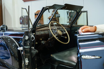 Fototapeta premium Close-up view of vintage convertible car interior, focusing on dashboard and steering wheel. Light-colored steering wheel with chrome accents contrasts with dark brown and black leather materials.