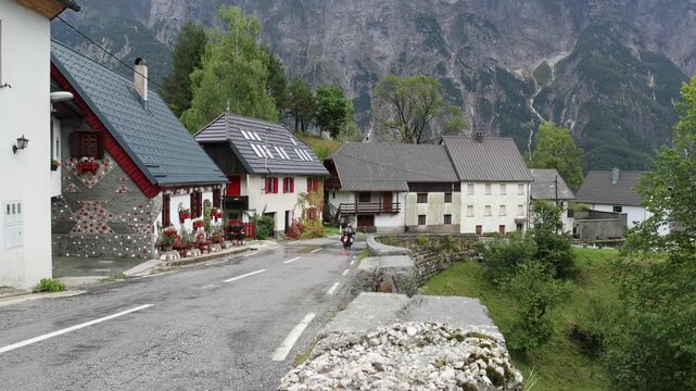 motorcycle driving down wet rainy road in small village on the italian slovenia border in the julian alps (slovenia europe) european travel destination touring houses town
