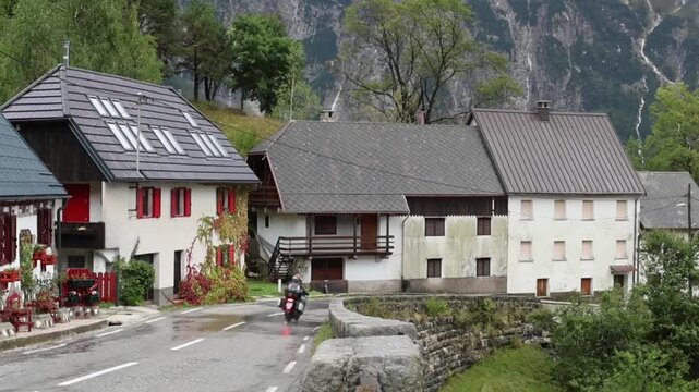 motorcycle driving down wet rainy road in small village on the italian slovenia border in the julian alps (slovenia europe) european travel destination touring houses town