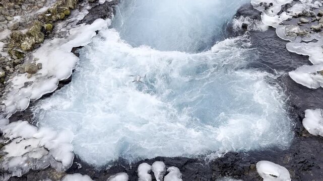 Slow motion of drone flying over snowy Iceland waterfall, Bruarfoss, as it gushes down