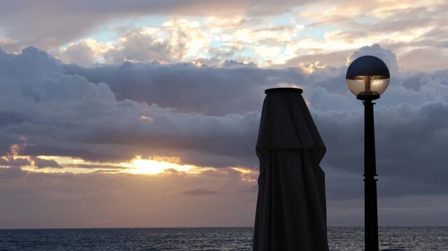 sunset timelapse Mediterranean sea Adriatic coast in Piran slovenia european travel tourism destination with street lamp streelight and closed umbrella after rain dramatic clouds sun shine time lapse 