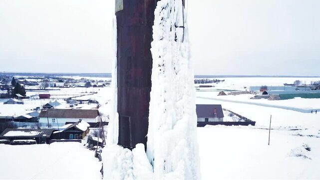 A frozen water tower. The water has turned to ice. It's abnormally cold. An ice-covered iron structure that holds water. An ice-covered iron water tower.