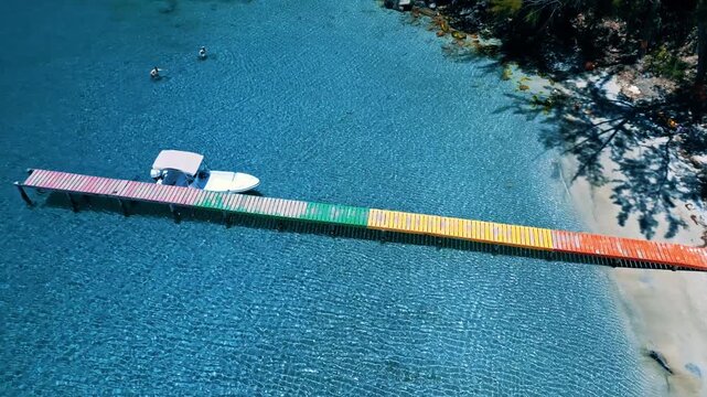 Aerial view of Deena Beach featuring a vibrant multicolored wooden pier extending into turquoise waters with a docked boat and lush tropical trees Guanaja, Bay Islands Department, Honduras.