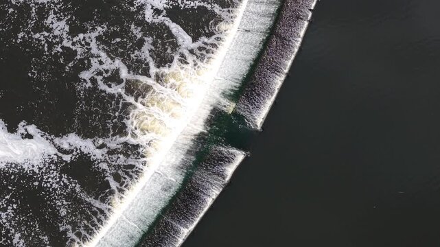 Aerial view of Knottingley Weir and Hydroelectric Power Plant with rushing white water and foam over the concrete structure in Knottingley, England, United Kingdom.