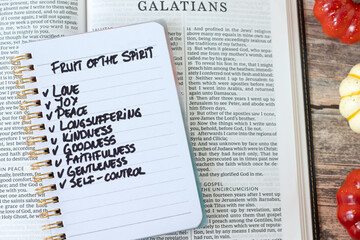Fototapeta premium Christian fruit of the spirit (love, joy, peace) text in a notebook with holy bible on wooden background. Top view. Biblical concept.
