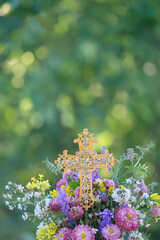 beautiful golden openwork cross with rhinestones and meadow flowers bouquet close up outdoor, nature background. symbol of Christianity religion, faith in God, Church holidays. template for design