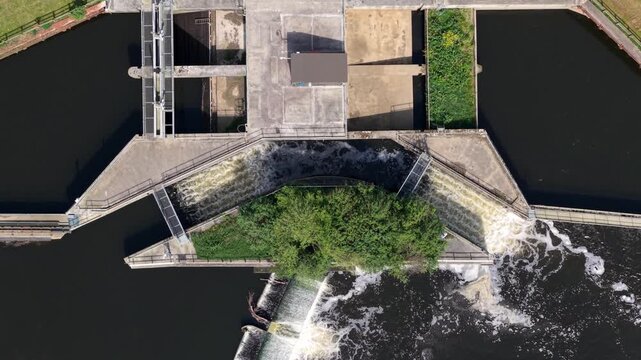 Aerial view of Knottingley Weir and Hydroelectric Power Plant with rushing water flowing over the concrete dam structure and lush green trees Knottingley, England, United Kingdom.