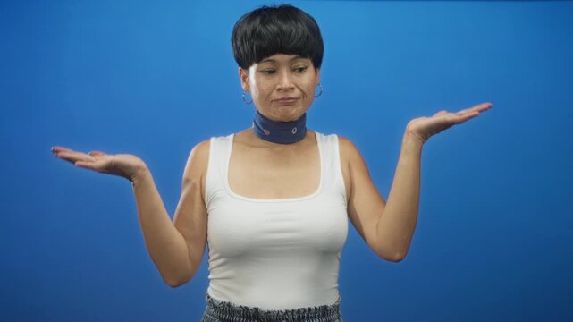 Woman shrugs with palms up and looks uncertain, wearing white tank top and neck scarf in studio; uncertainty indecision.