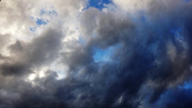 Dark clouds roll across blue sky. Stormy atmosphere with dramatic light. Clouds move slowly, changing shape. Sky shows deep blues and gray tones. No animals or plants visible