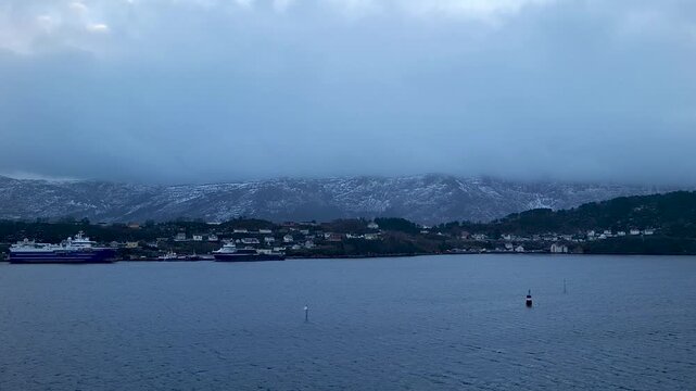 Alesund Norway jan 14 2025 Moody Winter Harbor With Ferries Docked Below Snowy Mountains And Overcast Sky