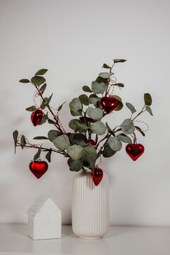 closeup eucalyptus branches decorated with red heart ornaments for christmas .vertical festive card
