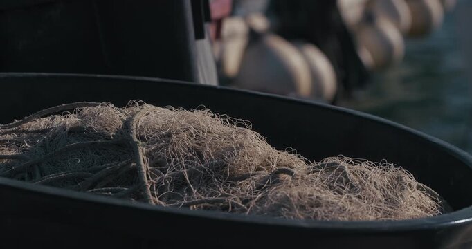 Close-up of fishing net piled inside a container with blurred harbor background.