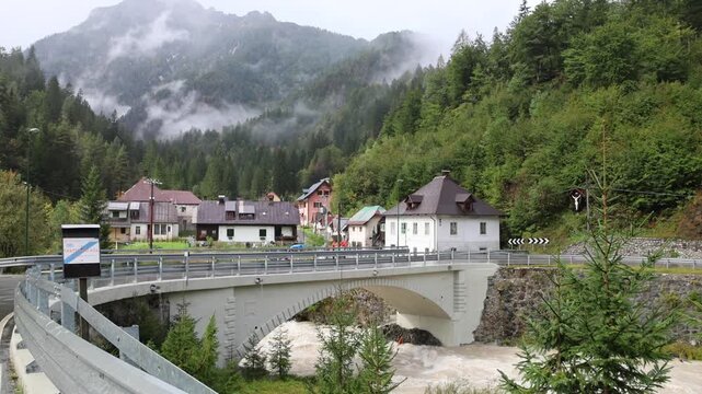 water rushing in a mountain river in small town in rural slovenia europe near italian border with italy (rain rainy day mist misty fog foggy) buildings village julian alps