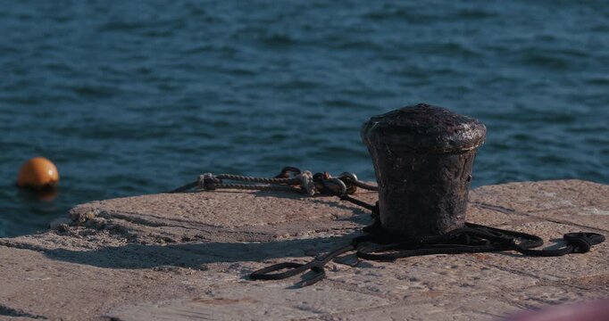 Rusty mooring bollard with ropes on a concrete pier beside the sea in Rovinj, Istria, Croatia.