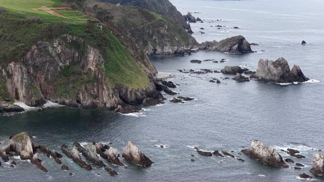 Aerial view of Silence Beach featuring steep green cliffs and sharp sea stacks emerging from the calm Atlantic waters in Asturias, Asturias, Spain.