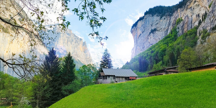 Beautiful alpine countryside landscape in Lauterbrunnen Valley, Bern Canton, Switzerland featuring a traditional Swiss farmhouse, green hills, dramatic rocky cliffs and the famous Staubbach Falls in t