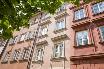 Facade of historic tenement buildings in Warsaw Old Town Poland. Low angle view of traditional architecture with colorful plaster, window frames and cornices on a sunny day. © Lina