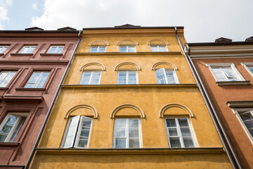 Facade of historic tenement buildings in Warsaw Old Town Poland. Low angle view of traditional architecture with colorful plaster, window frames and cornices on a sunny day. © Lina