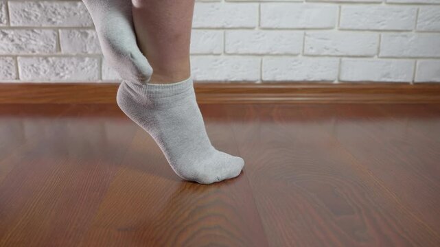 Person performing calf raises exercise. Close-up of a woman's legs in grey socks performing single-leg calf raises, strengthening his calf muscles and improving his balance