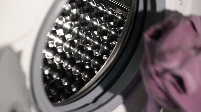 Woman putting colorful clothes in washing machine. Close-up of a person's hand loading dirty laundry into the shiny steel drum of a modern washing machine before starting the wash cycle