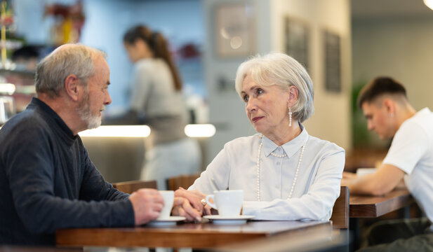 Joyful elderly couple on a date in a cozy coffee shop, they have a nice conversation and discuss joint plans.