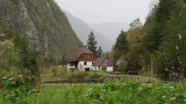 rain falling in on small house along the road with plants moving in the foreground soca valley julian alps slovenia europe european iconic historic home trees mountains