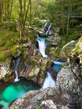 Beautiful Lepena Waterfalls in Sunikov vodni gaj, surrounded by mossy rocks and forest in Soca Valley. Turquoise pools and cascading crystal clear water in a pristine and peaceful alpine landscape.