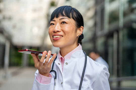 Female doctor dictating voice message on smart phone outdoors