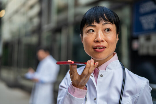 Female doctor dictating voice message on smart phone outdoors