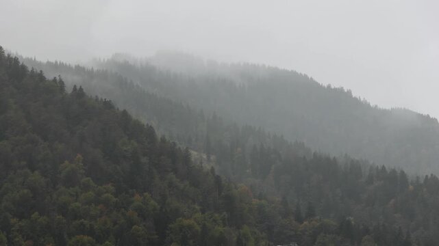 rain falling in the julian alps mountains in tarvisio, italy on the border with slovenia church rooftops trees hills mist weather raining storm alpine travel destination