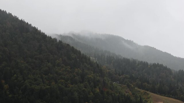 rain falling in the julian alps mountains in tarvisio, italy on the border with slovenia church rooftops trees hills mist weather raining storm alpine travel destination