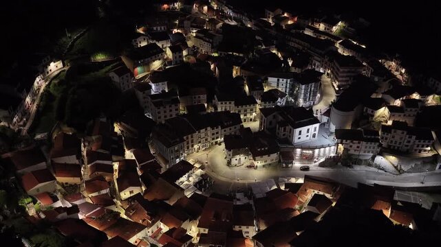 Aerial view of the coastal village at night with illuminated houses and winding streets nestled in the hills of Cudillero, Asturias, Spain.