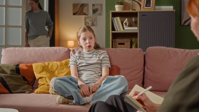 Preteen girl speaking openly to female psychologist sitting on couch in living room while mother observing conversation during family counselling session