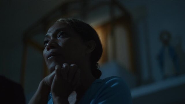 Devoted transgender woman is praying at night, her face illuminated by a soft, warm light