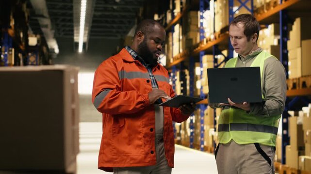 Diverse warehouse team, updating parcel tracking software, with laptop and tablet, typing shipment details and status for dispatch information. Staff overseeing order fulfillment for delivery.