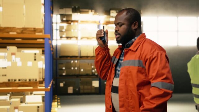 Depot employee communicating through portable walkie-talkie device near cardboard boxes racks. Equipment ensures teamwork safety and accurate cargo movement across warehouse infrastructure.
